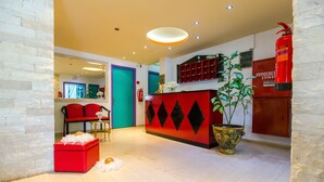 Un moderno vestíbulo con un mostrador de recepción rojo, una puerta verde azulado y un extintor.