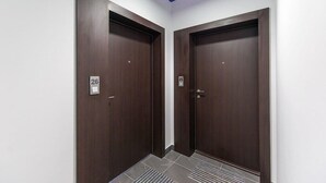 Duas portas de madeira escura com os números 25 e 26, indicando os números dos quartos, em um corredor com piso ladrilhado e uma luminária azul no teto.