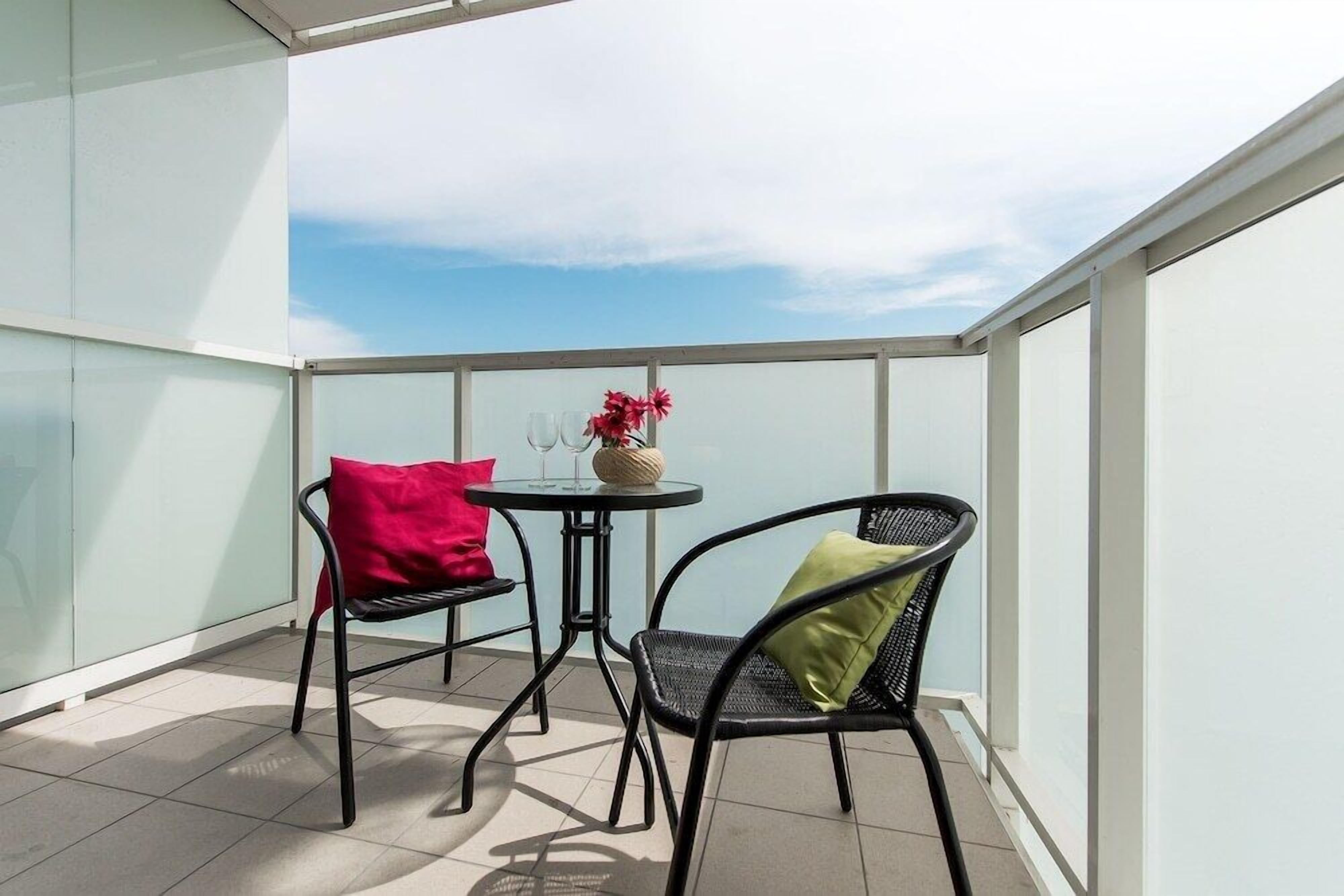 A balcony with two chairs, a small round table, and a vase with flowers.