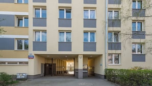 Un edificio de varios pisos con entrada central, un cartel que indica la planta baja y un camino de acceso con portones.