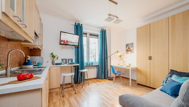 Un espacio habitable compacto con kitchenette, comedor y zona de estar con sofá y sillón.