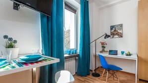 Una cocina moderna con una mesa de comedor, sillas, un ventanal con cortinas, un radiador y un escritorio con silla y laptop.