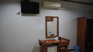 A small room with a wooden desk, a mirror, a television mounted on the wall, and a small refrigerator. - Country Inn 304 (Si Maha Phot)