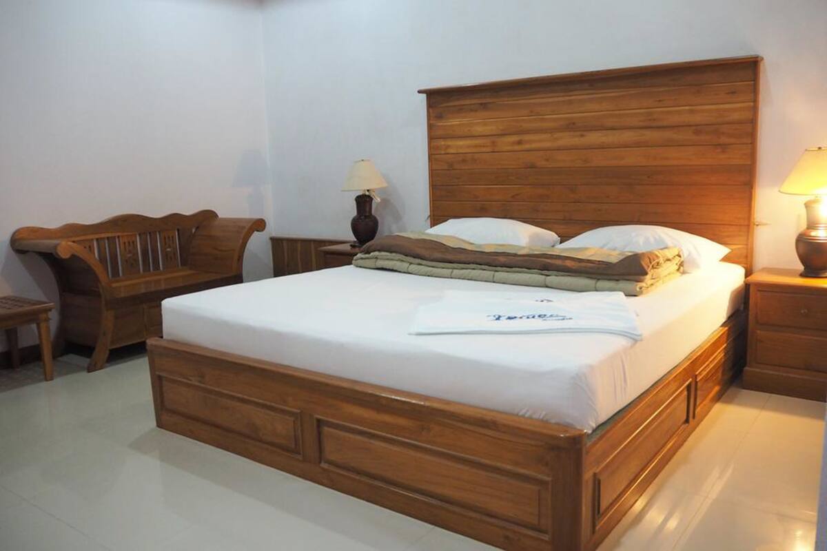A wooden bed with a headboard, a nightstand with a lamp, and a wooden bench.