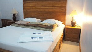 Uma cama bem arrumada com cabeceira de madeira, duas mesas de cabeceira com luminárias, e um espalha-cama branco com toalha e uma peça de roupa dobrada sobre a cama.