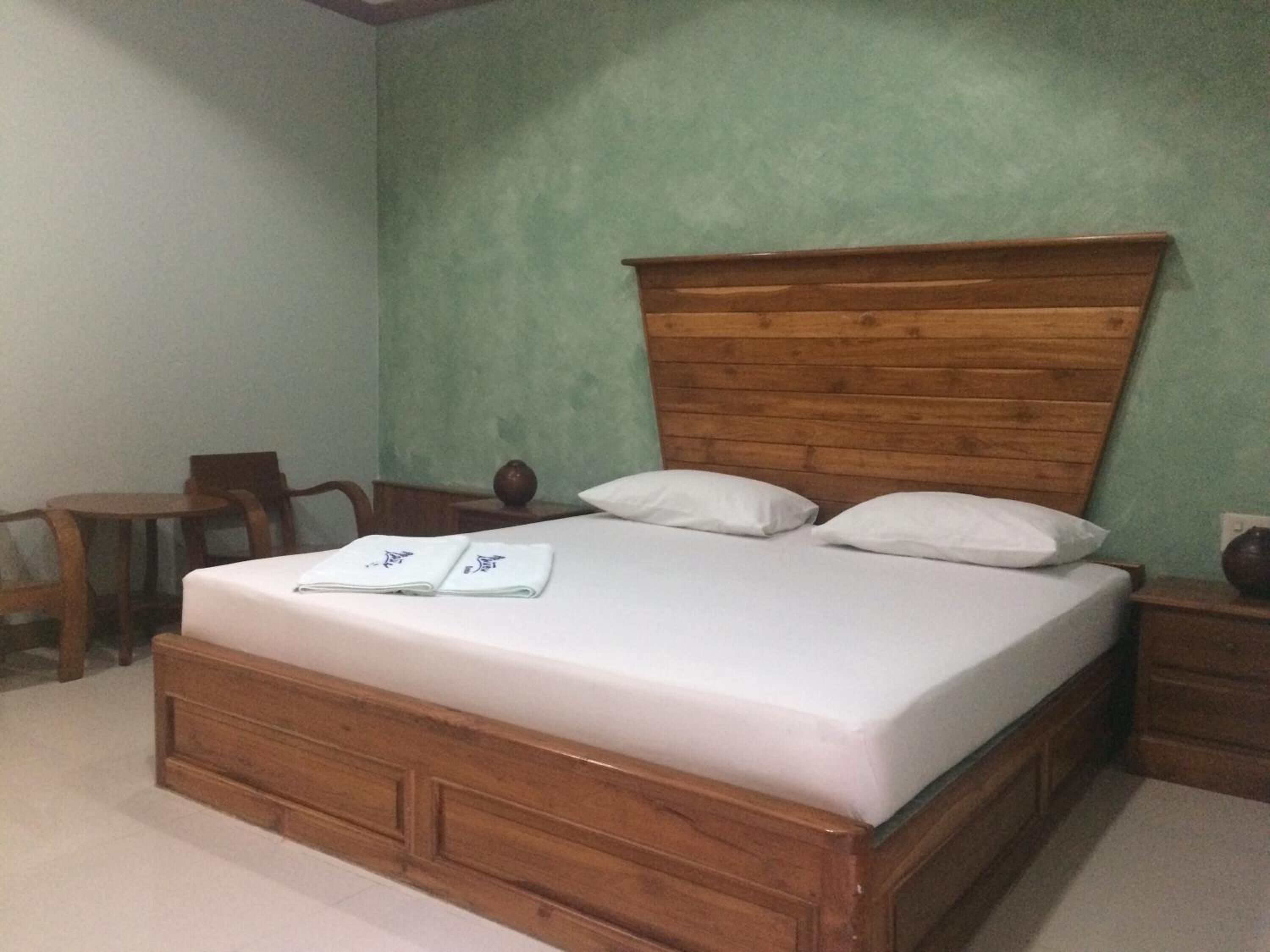 A neatly made bed with a wooden headboard in a room with green walls and a small table.