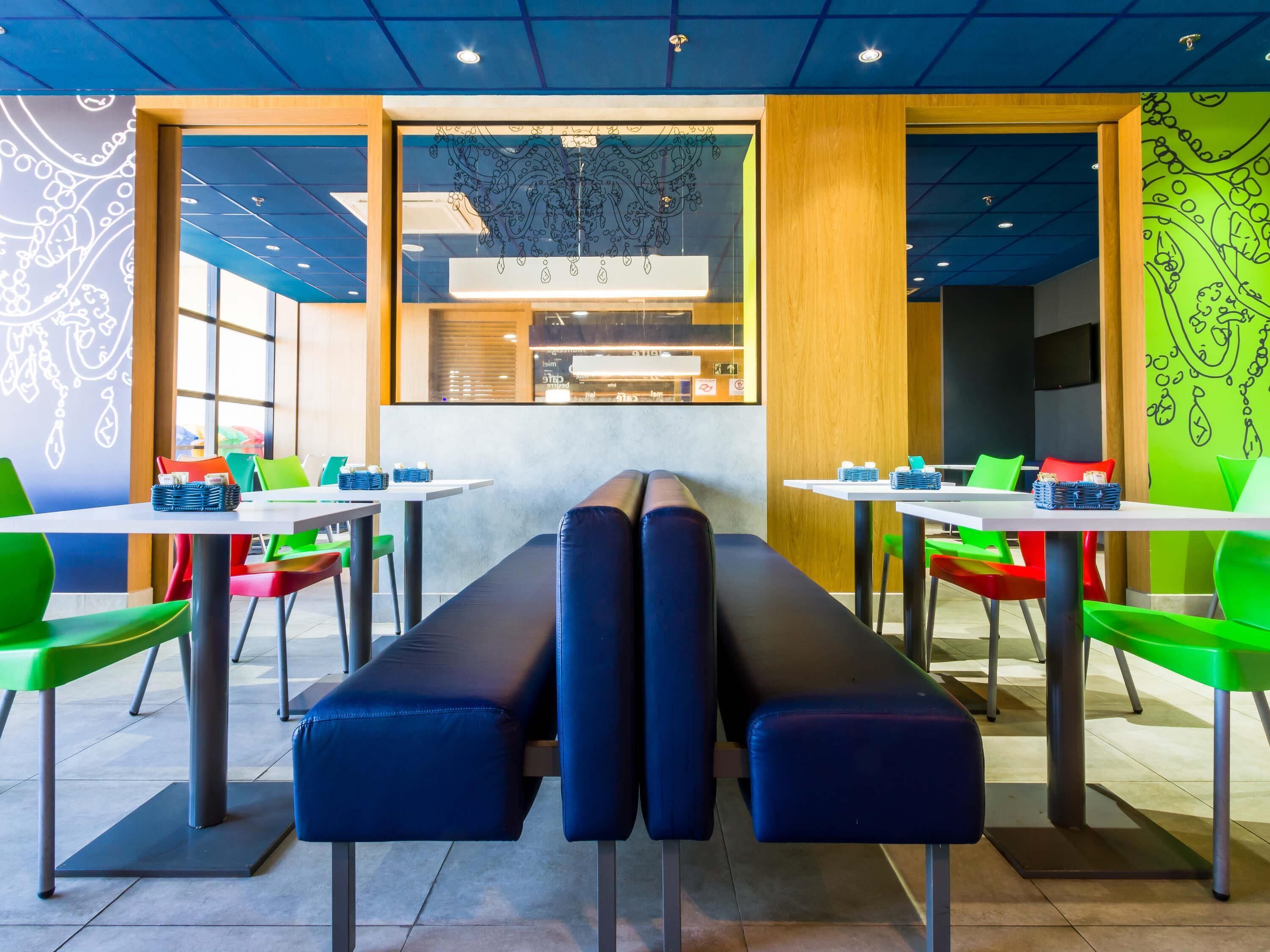 Un interior de restaurante moderno con cabinas, mesas altas y sillas coloridas.