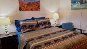 Un dormitorio con cama, dos mesitas de noche con lámparas, una silla y dos cuadros en la pared.