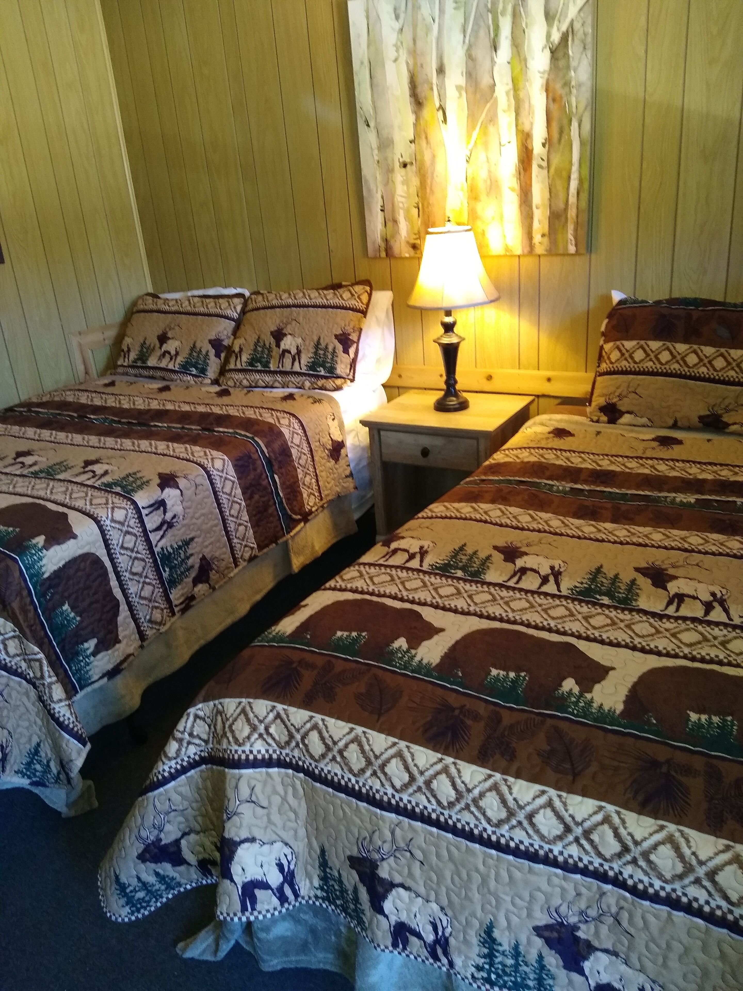 A room with two beds, each with a patterned blanket featuring animal prints. There is a nightstand with a lamp between the beds.