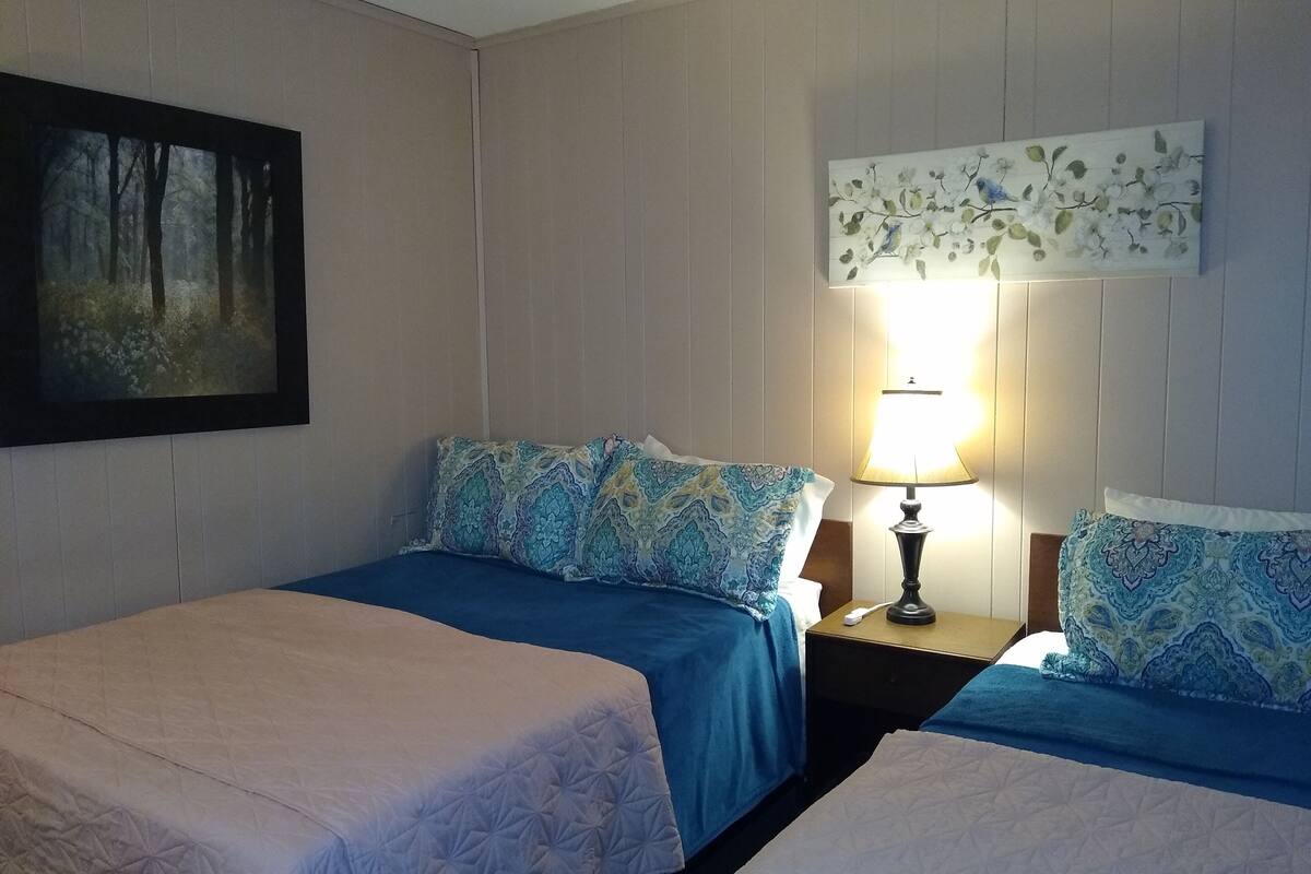A hotel room with two beds, a nightstand with a lamp, a painting on the wall, and a floral artwork above the bed.