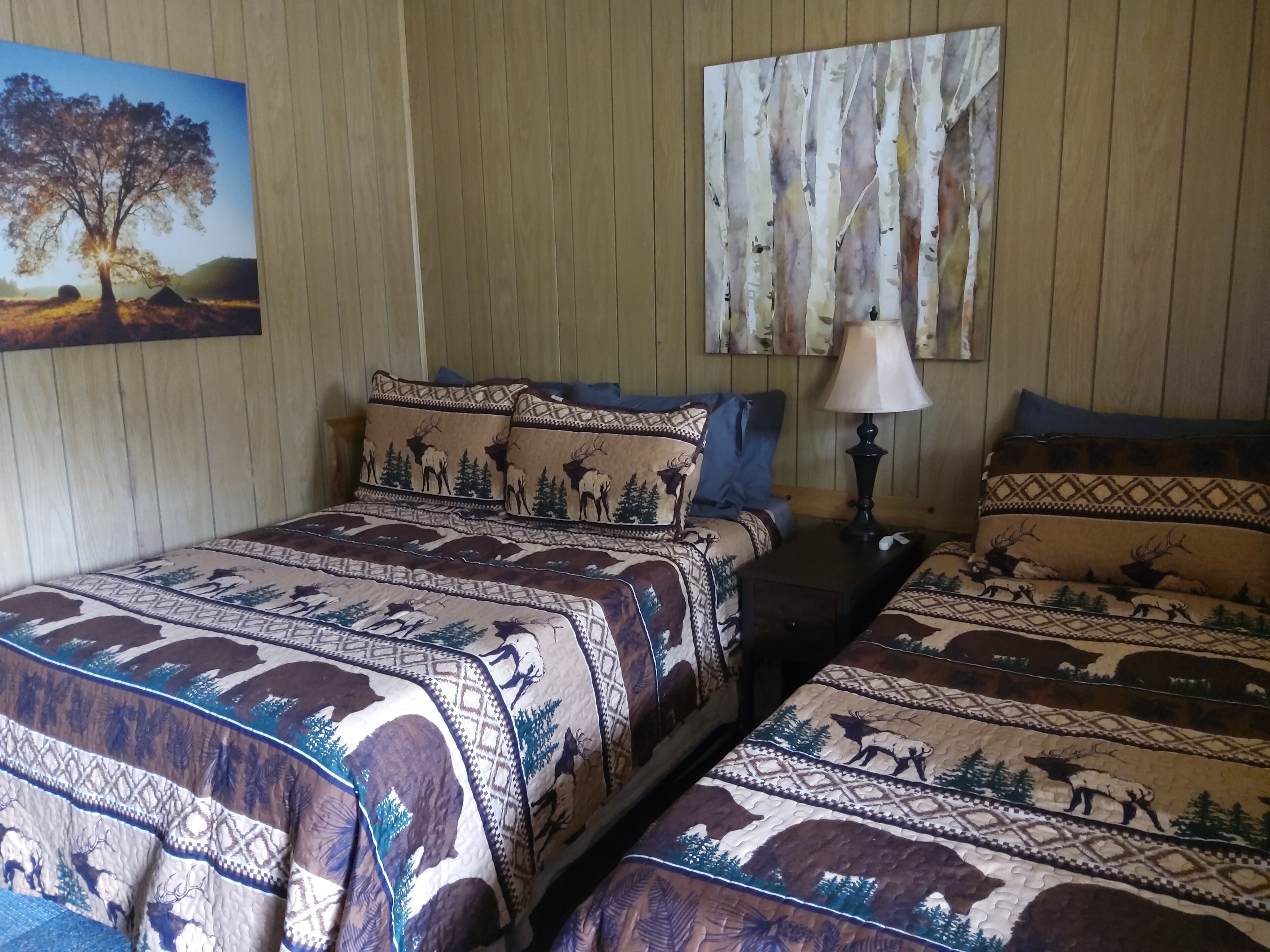 A room with two beds, each with patterned bedding featuring animal prints. There is a painting on the wall and a lamp on a bedside table.