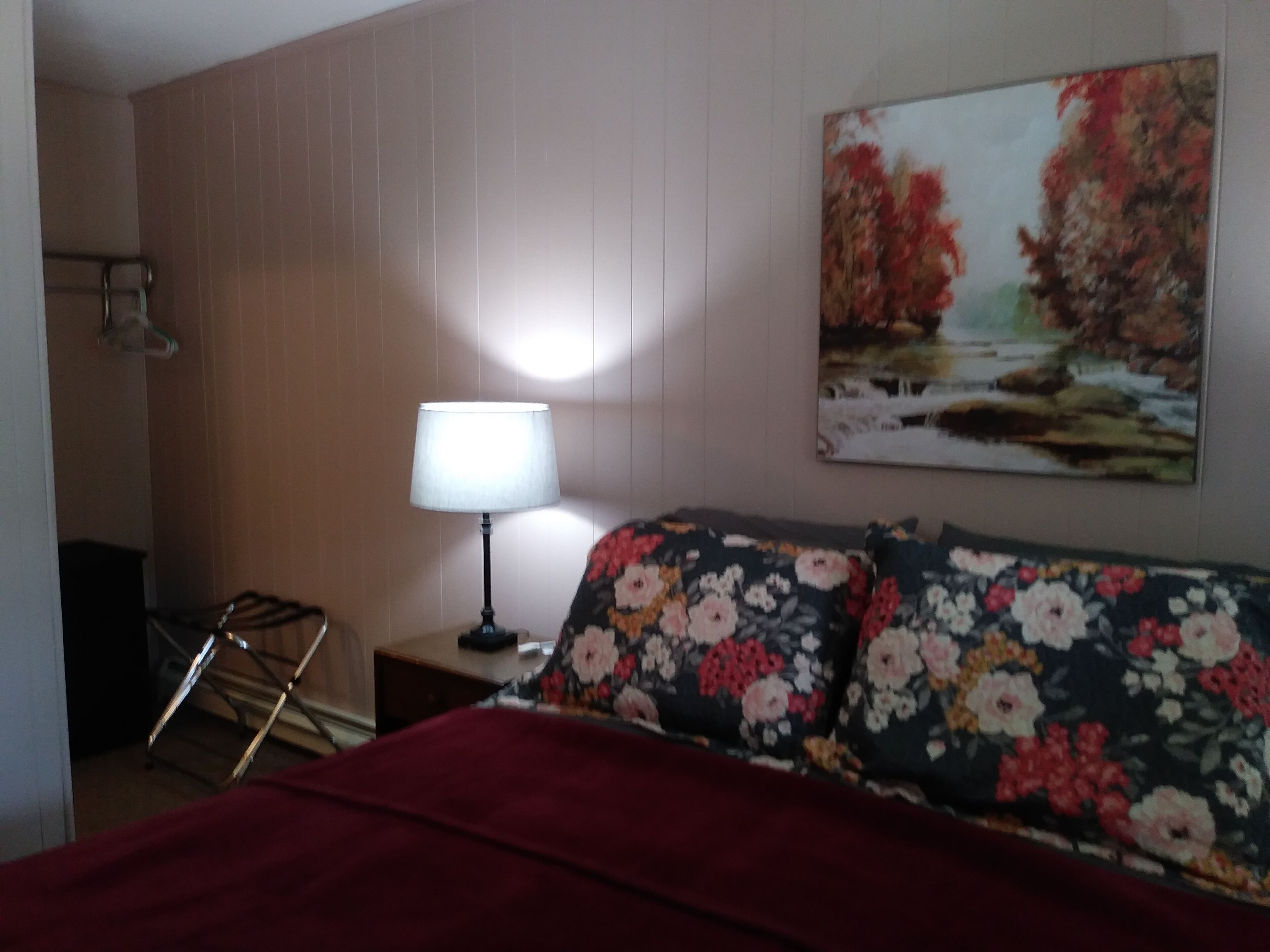A room with a bed, a nightstand with a lamp, a painting on the wall, and a window.