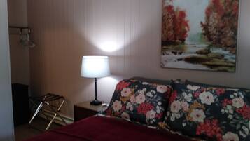 A room with a bed, a nightstand with a lamp, a painting on the wall, and a window.