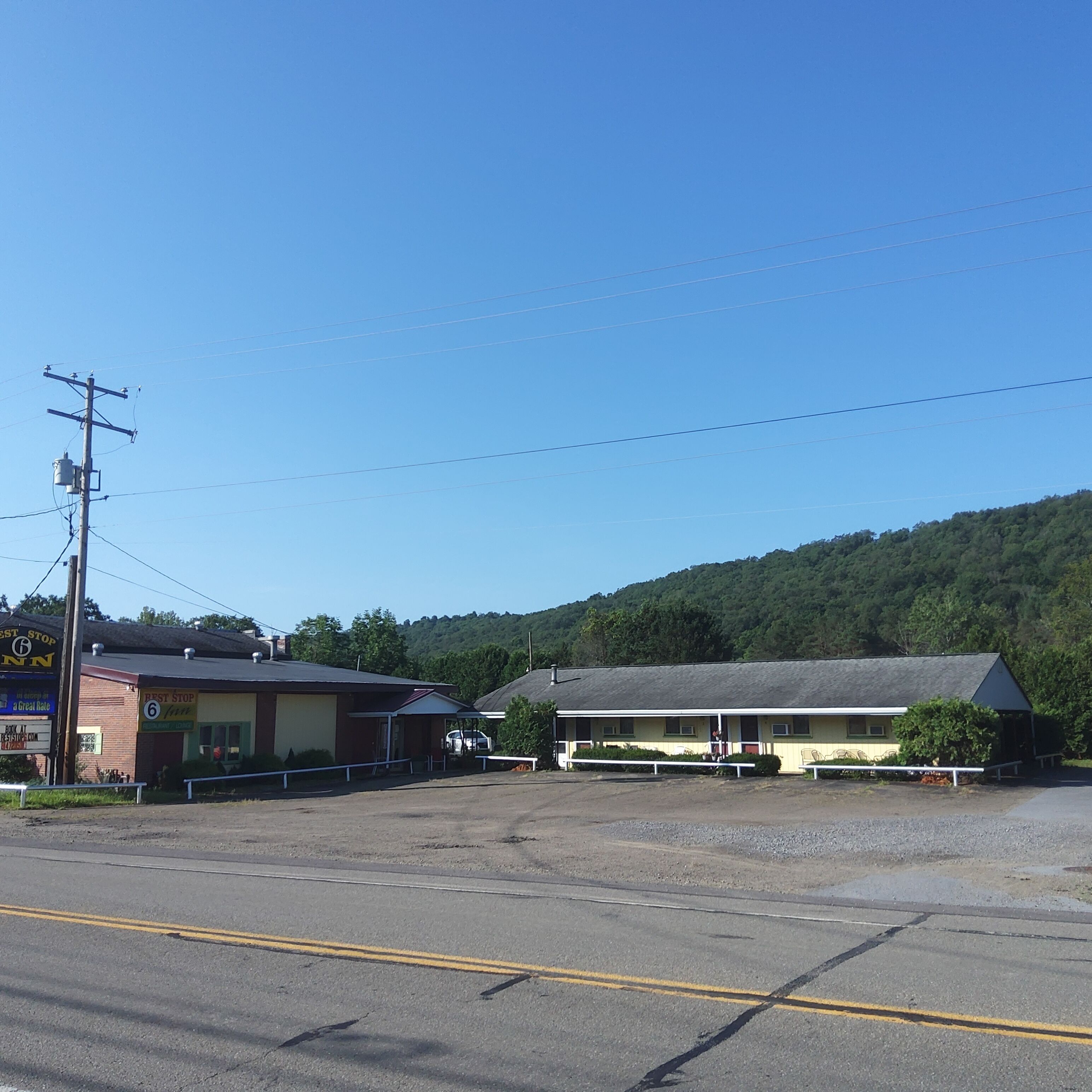 A motel with a large parking lot, a building with a sign that reads "Best Stop Inn", and a hill in the background.