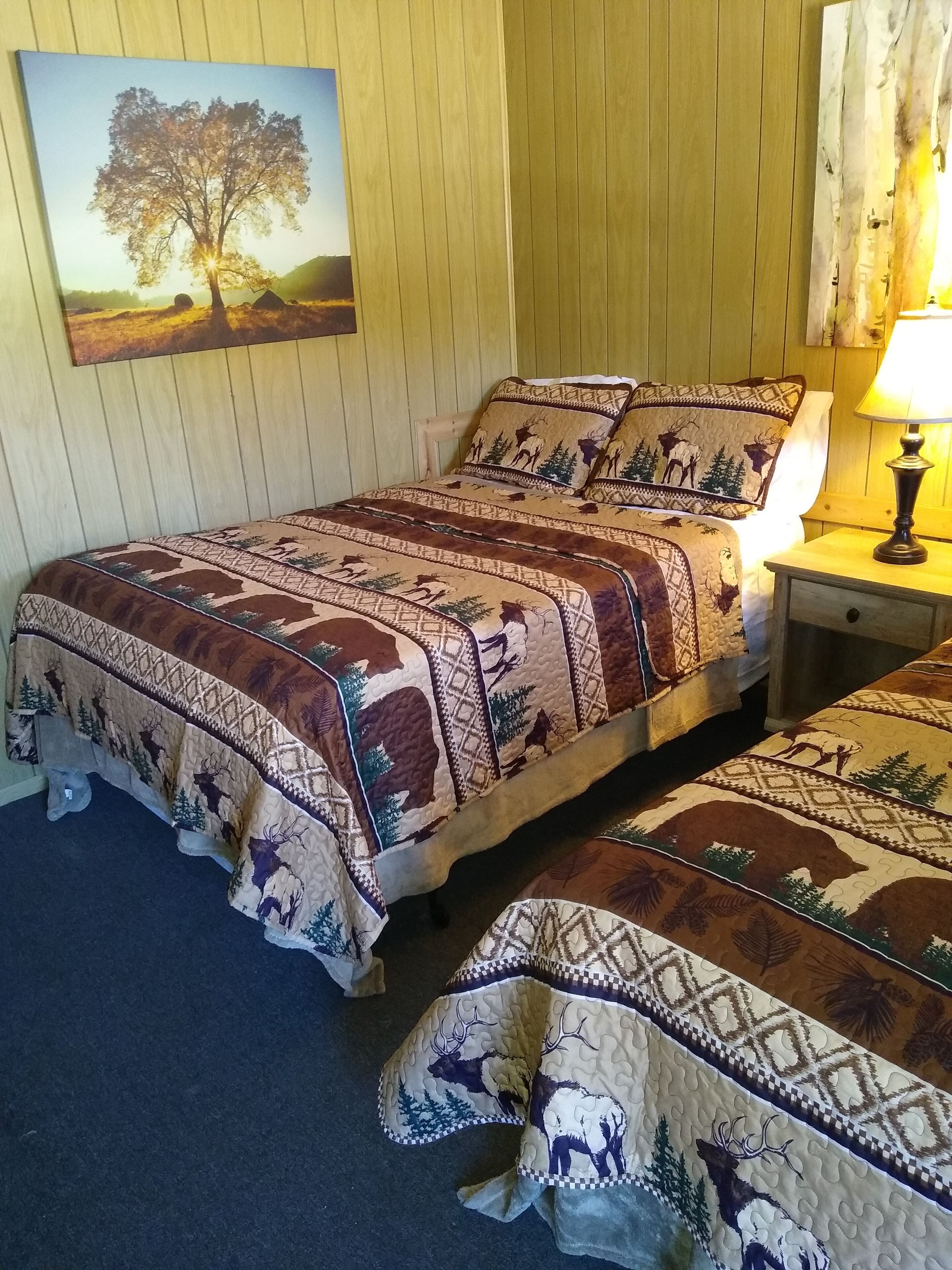 A room with a bed featuring a patterned quilt, a bedside table with a lamp, and a painting on the wall.