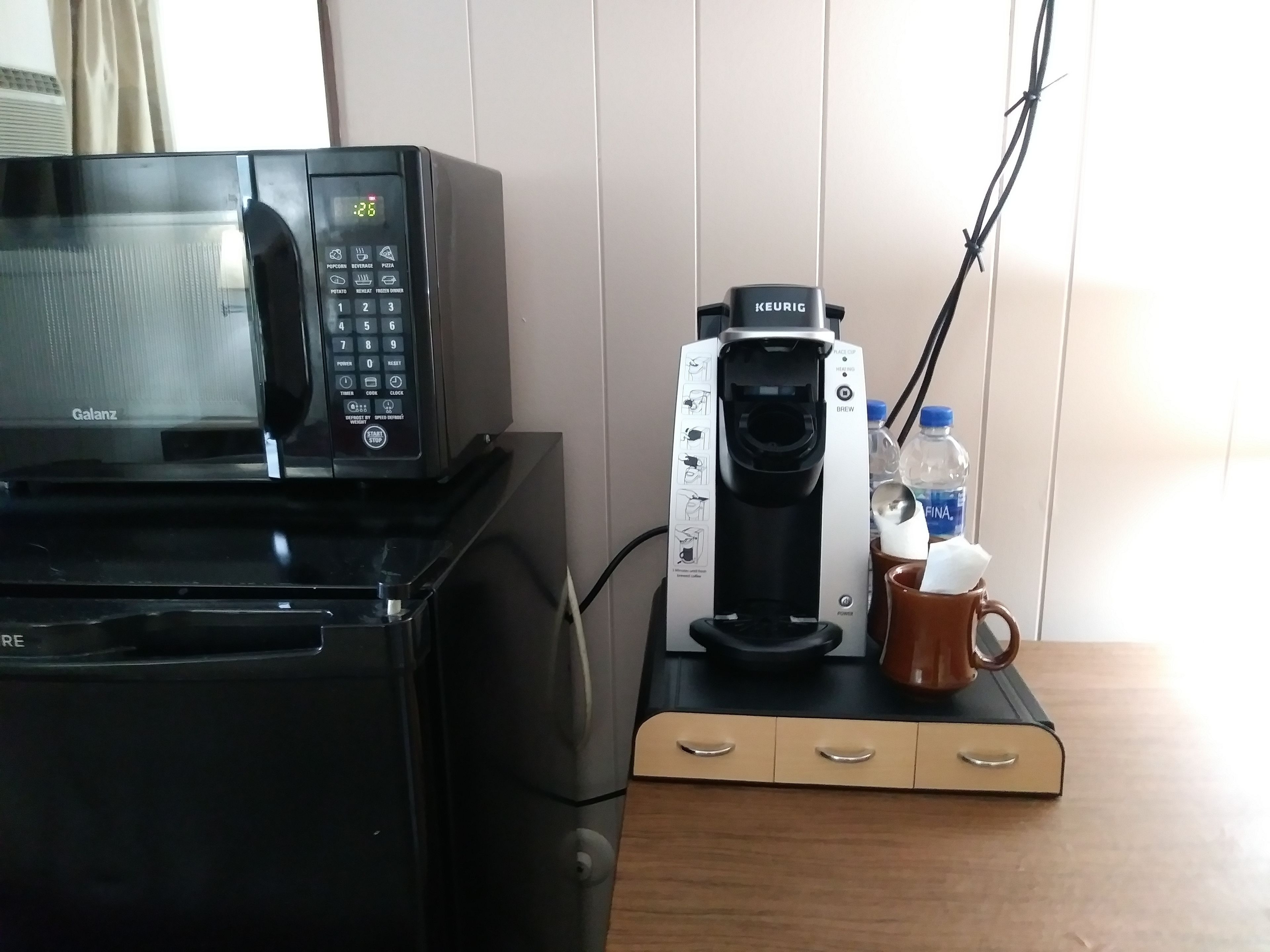 Een keukenhoek met een magnetron, koffiezetapparaat en een mok op een houten aanrecht.