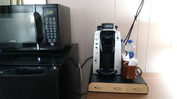 Een keukenhoek met een magnetron, koffiezetapparaat en een mok op een houten aanrecht.
