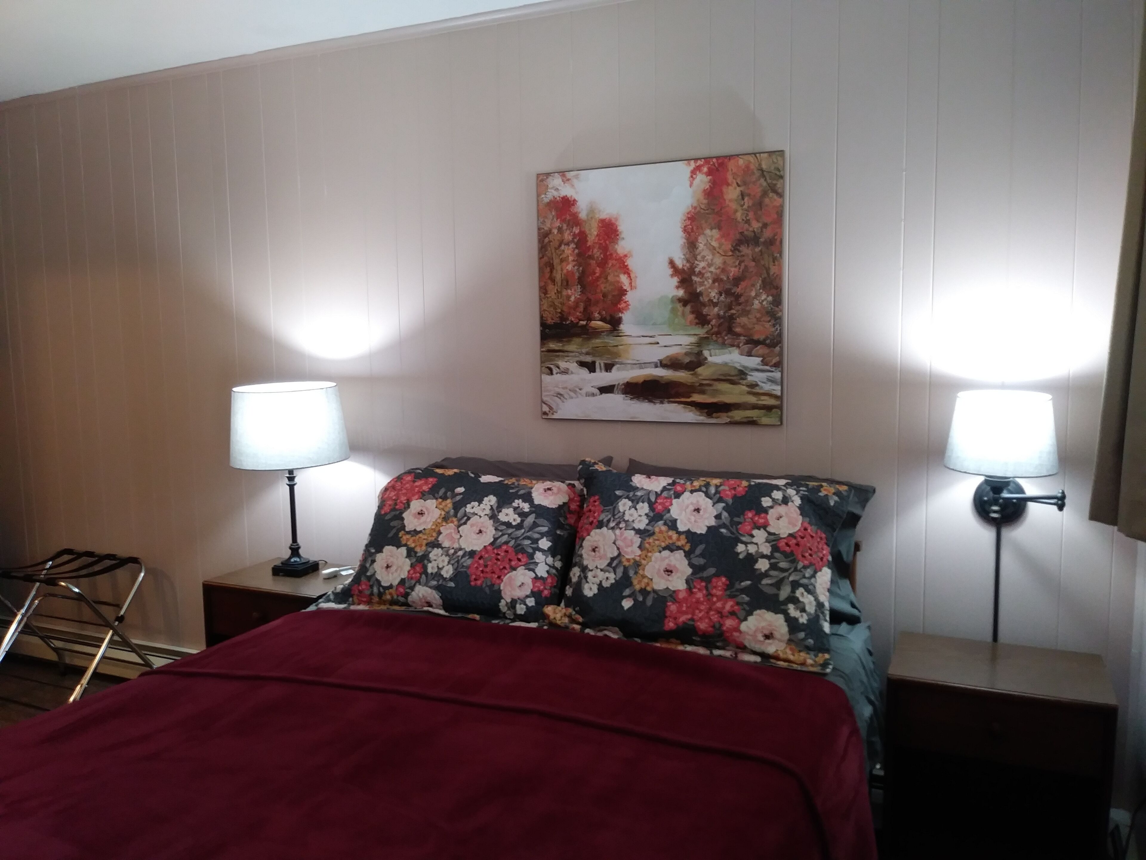 Habitación de hotel con cama, dos lámparas de noche, un cuadro en la pared y cabecero de madera.