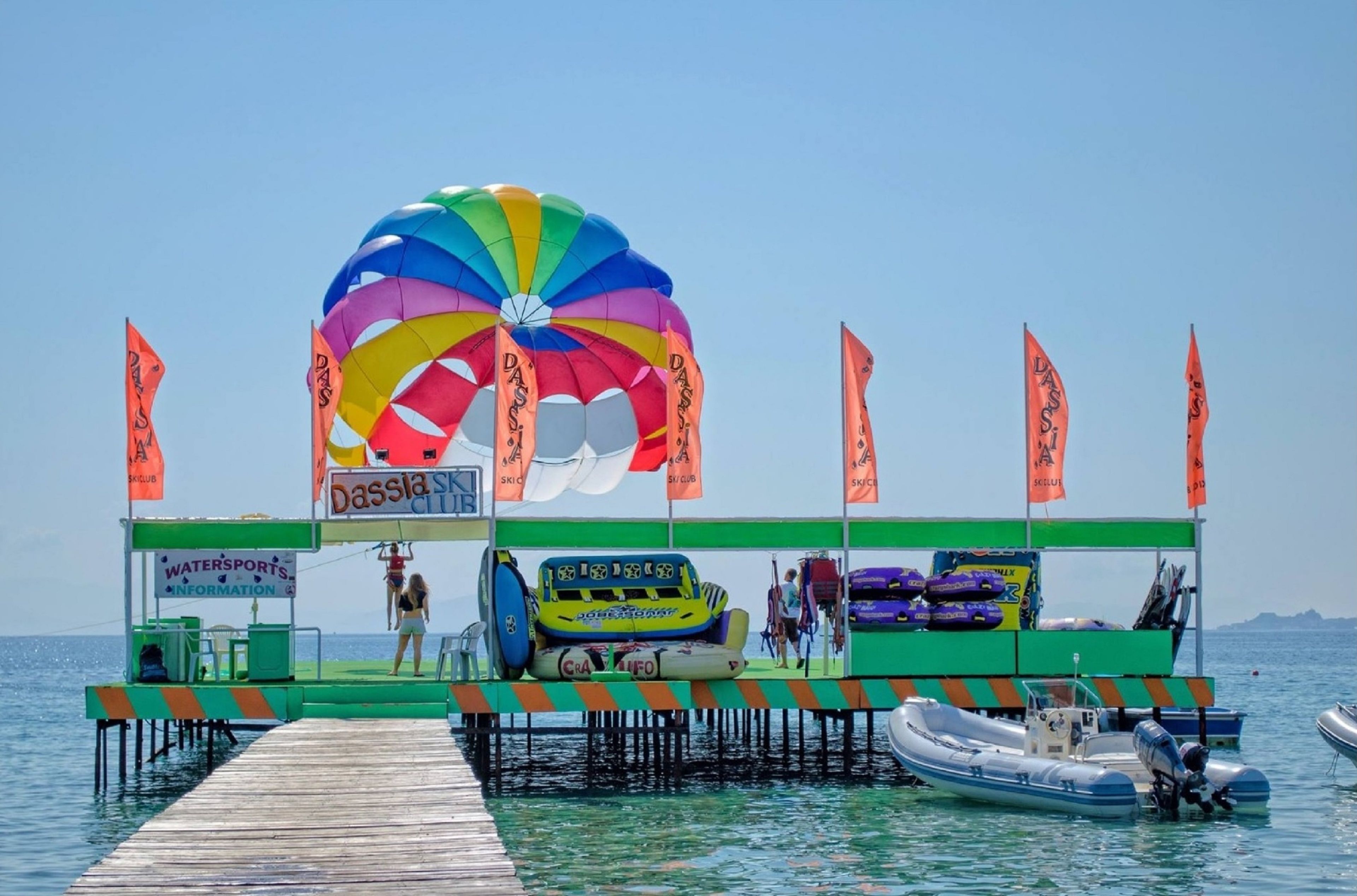 Un área de deportes acuáticos con paracaídas, botes inflables y un muelle.