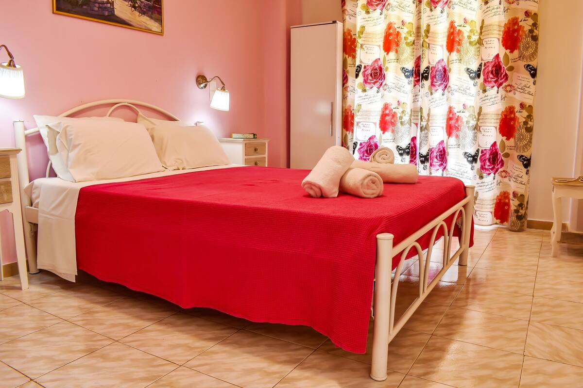 A neatly made bed with a red bedspread, a white headboard, and two bedside lamps.