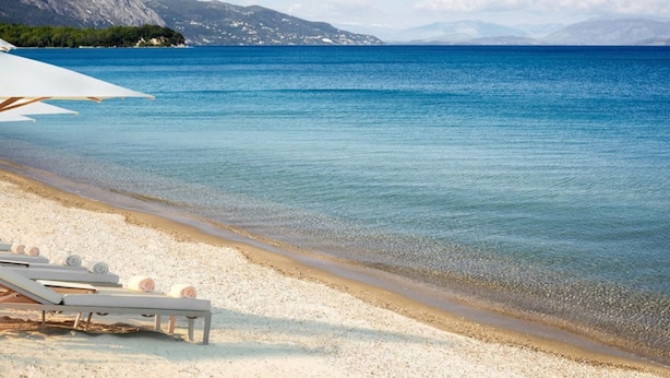 A beach with clear blue water, a sandy shore, and a row of sun loungers with umbrellas.
