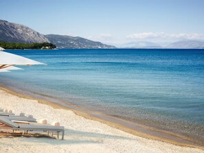 Une plage avec une eau d’un bleu limpide, un rivage sablonneux et une rangée de transats protégés par des parasols.