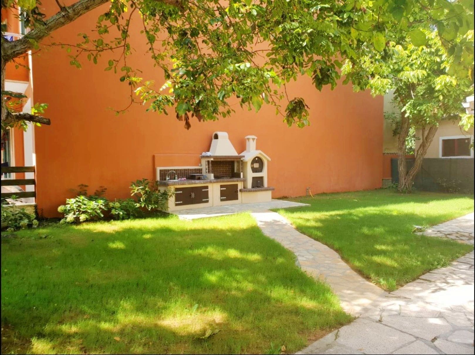 Un jardin avec un espace barbecue, un chemin de pierres et une pelouse bien entretenue.