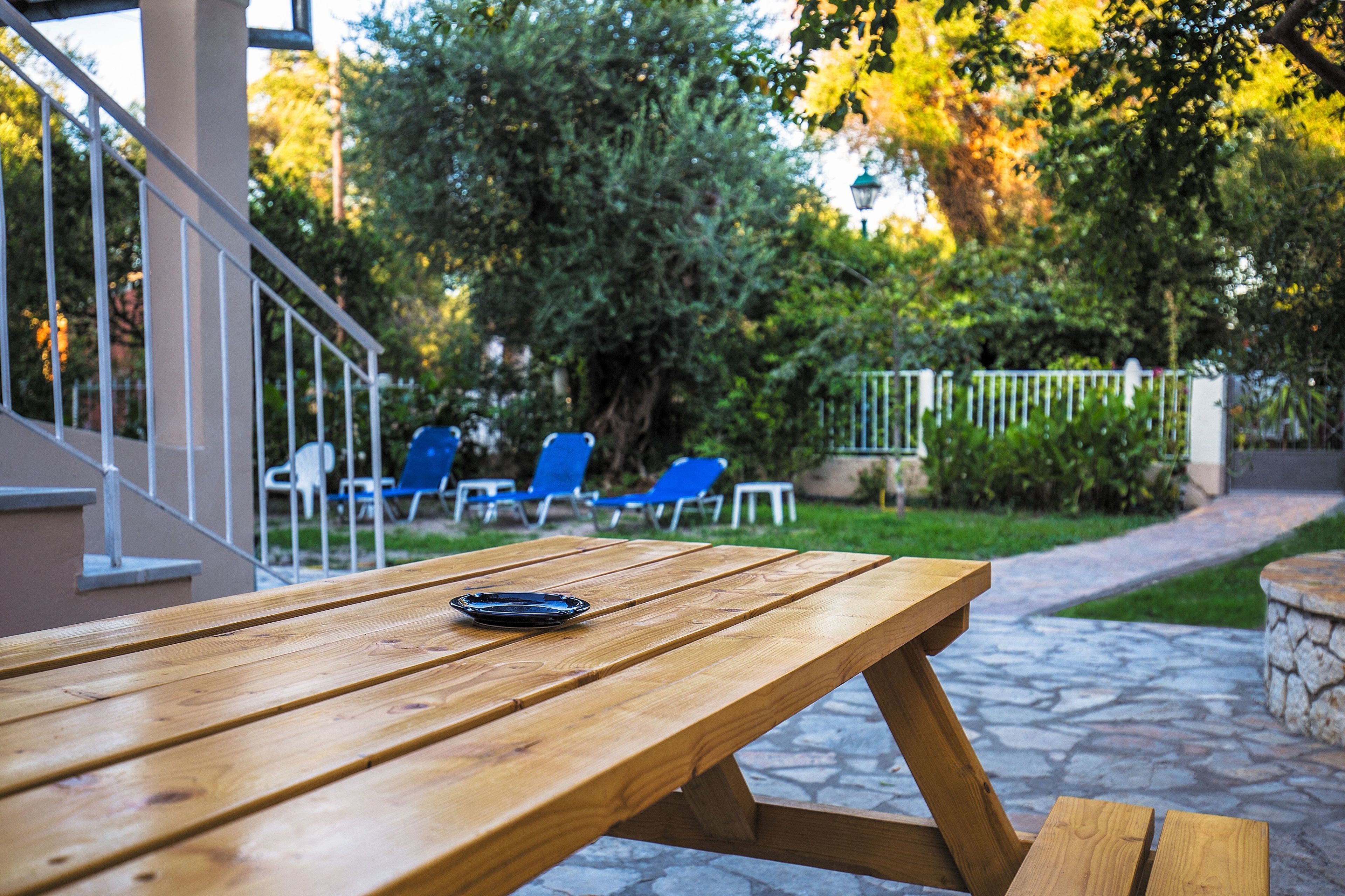 Een houten picknicktafel met een bord erop, omringd door blauwe stoelen en een pad van stenen.