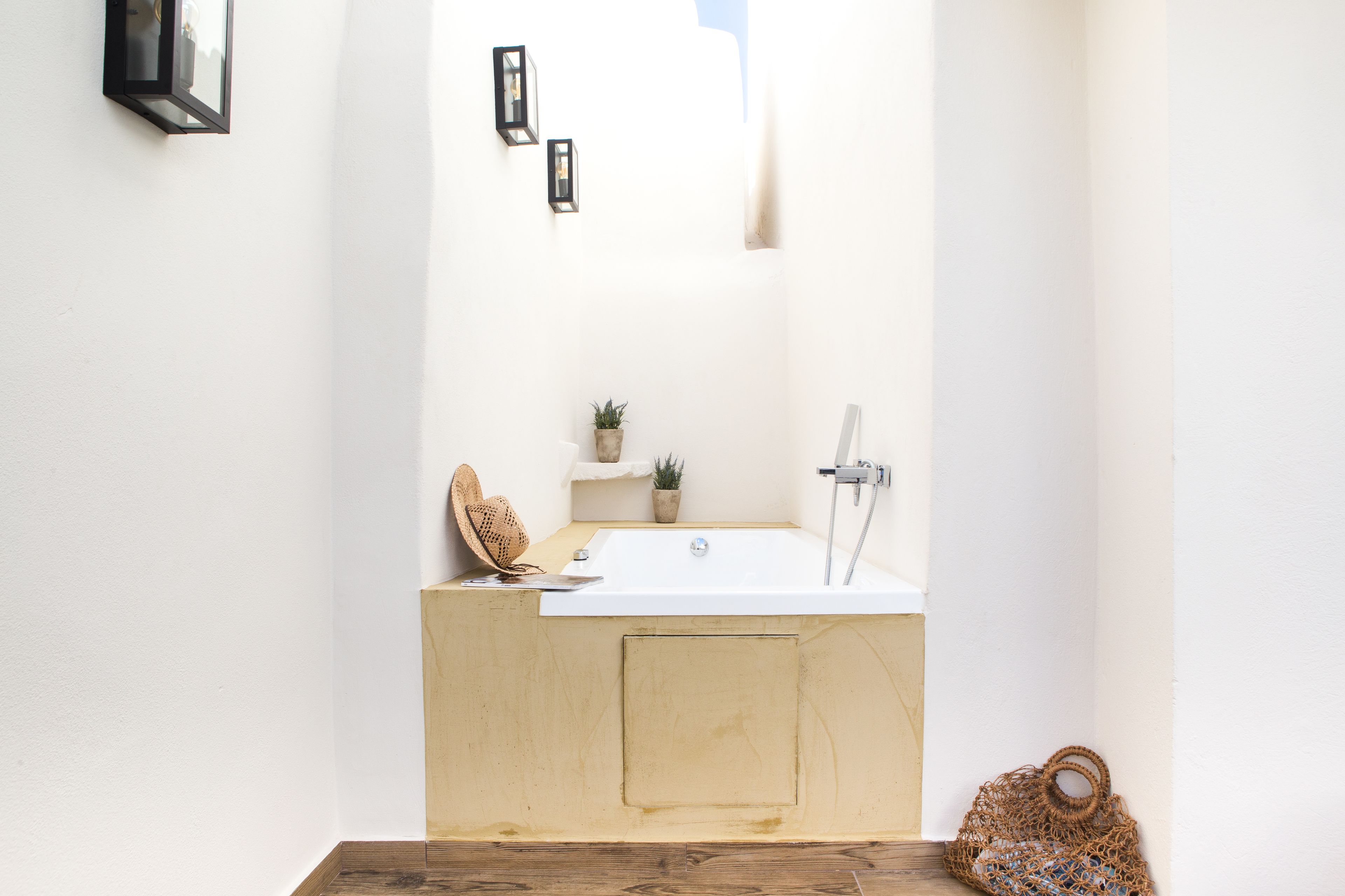 Een badkamer met een houten wastafelmeubel, een witte wasbak, een douche en een klein plankje met planten.
