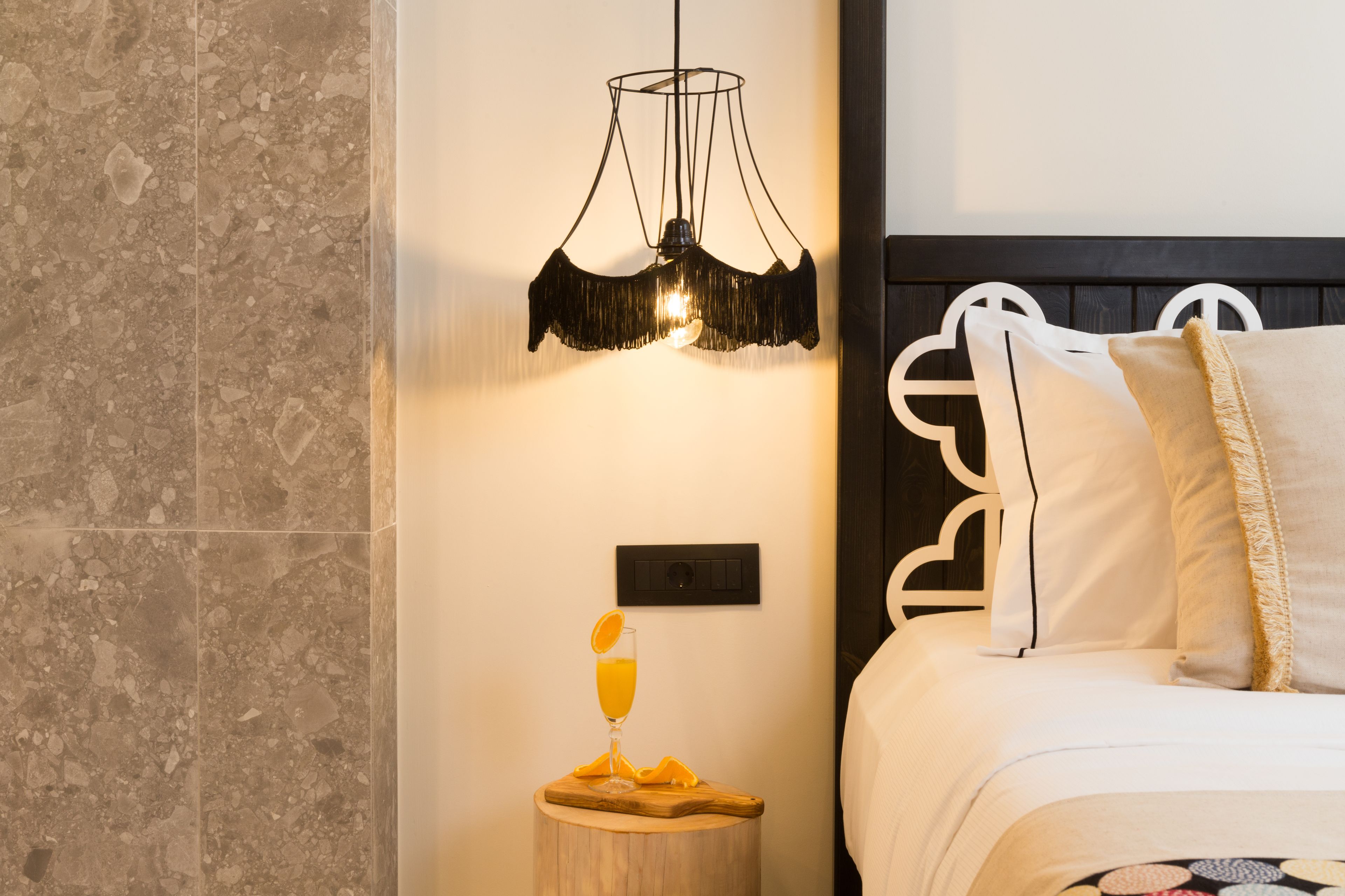 A bedroom with a bed, a bedside table with a glass of orange juice, a wall-mounted light fixture, and a textured wall.