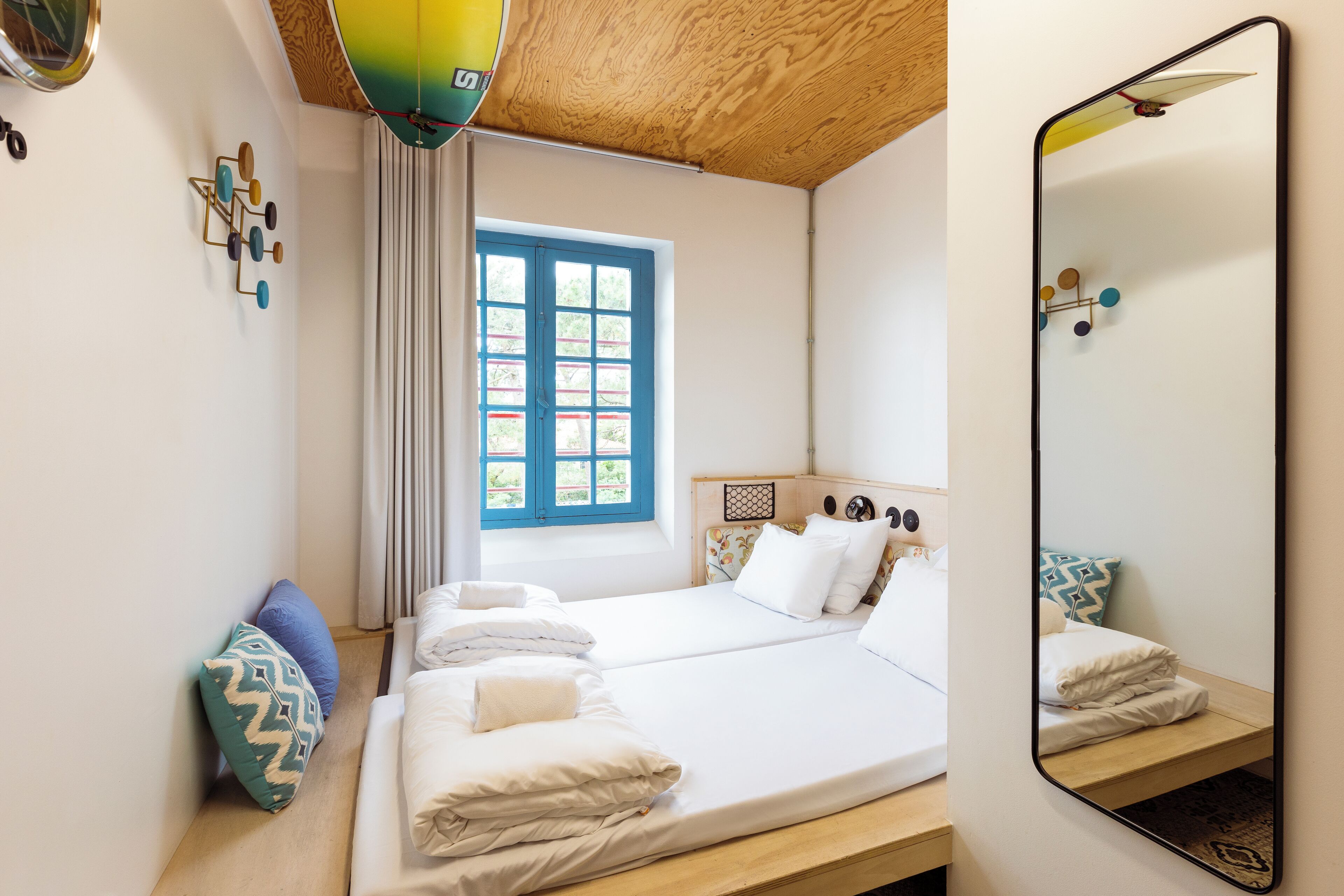 A bedroom with a bed, a window, a mirror, and a wooden ceiling.