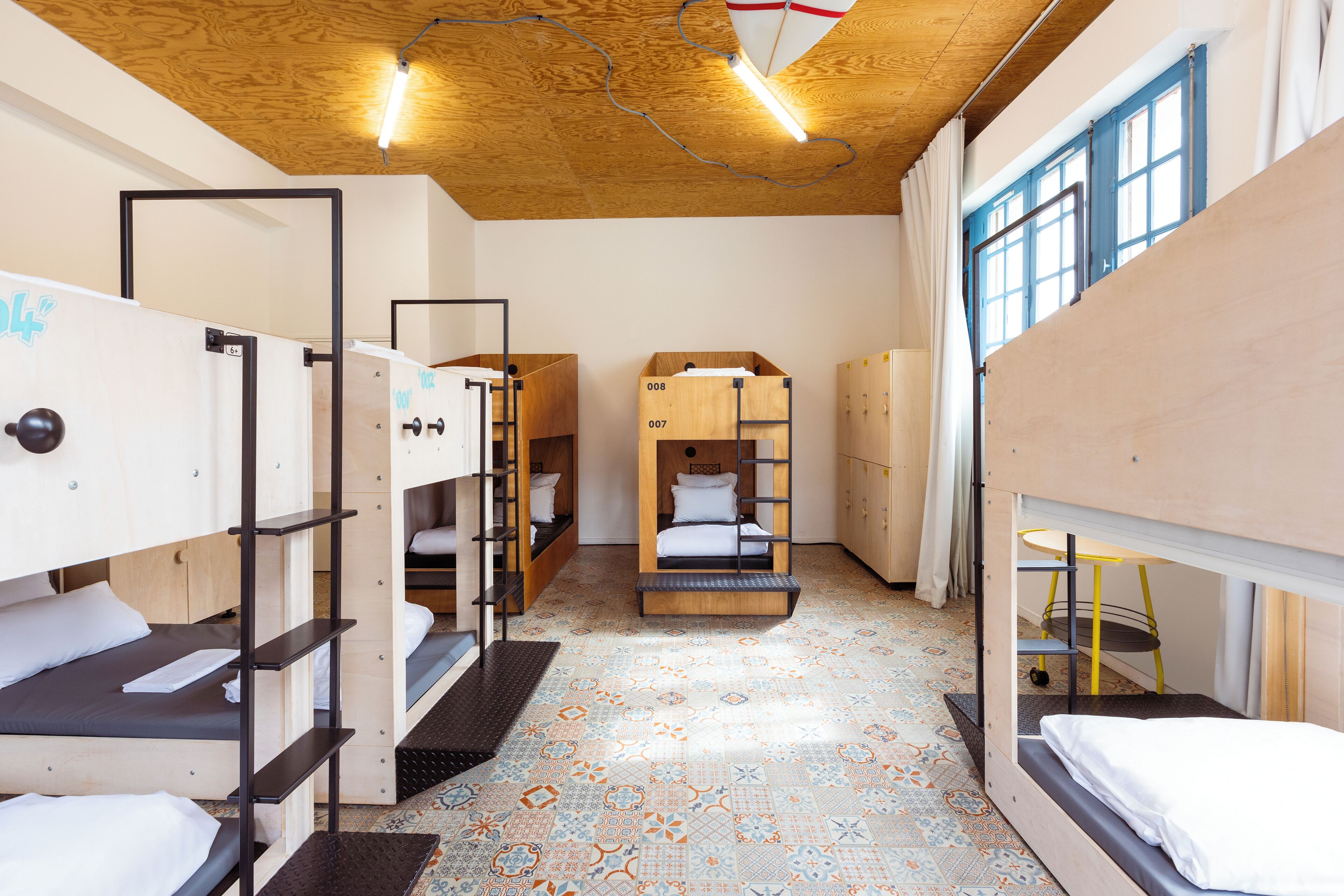 Une chambre de type dortoir avec des lits superposés, un sol à motifs et un plafond en bois.