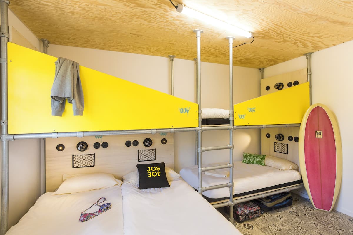 Ein Schlafraum mit Etagenbetten, einem Surfbrett und einem Handtuch an der Wand.