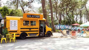 Un camión de comida amarillo llamado 'Soul Kitchen' estacionado en un área exterior sombreada con sillas y mesas coloridas.