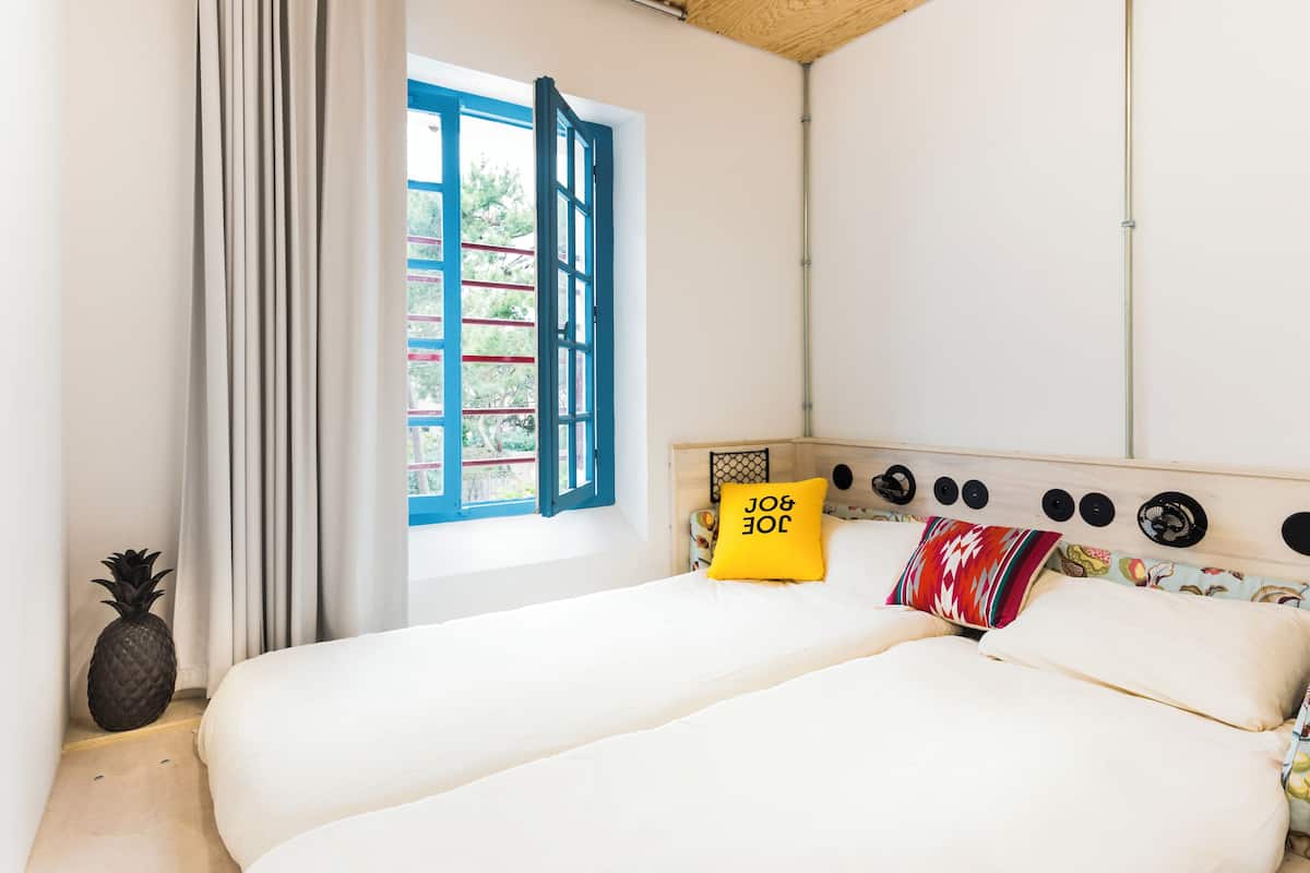 Ein Schlafzimmer mit einem Bett, einem Fenster mit blauen Rollläden, einer Ananas-Dekoration und einer Wand mit runden Verzierungen.