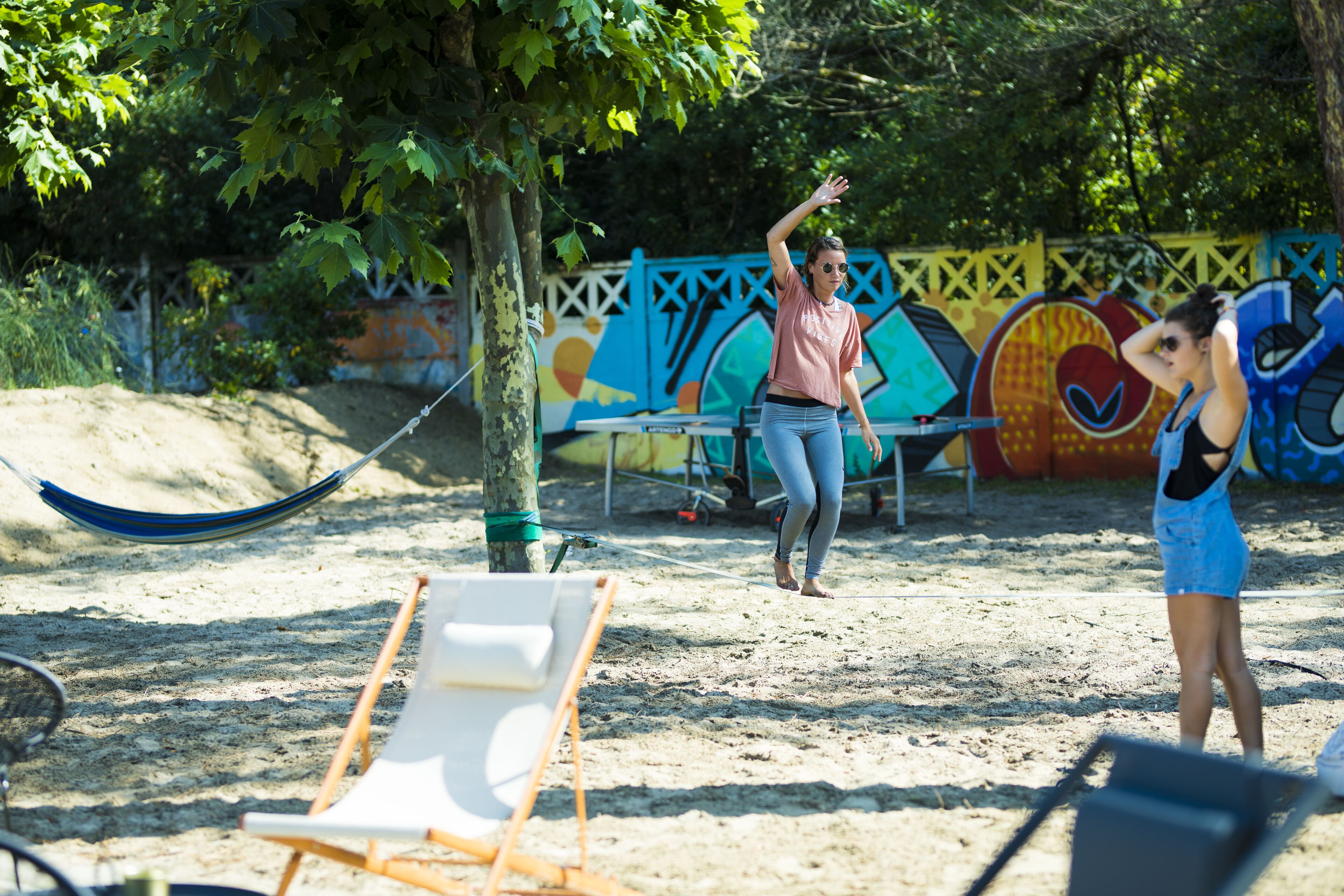 A sandy beach area with a hammock, a white lounge chair, and a colorful mural in the background.