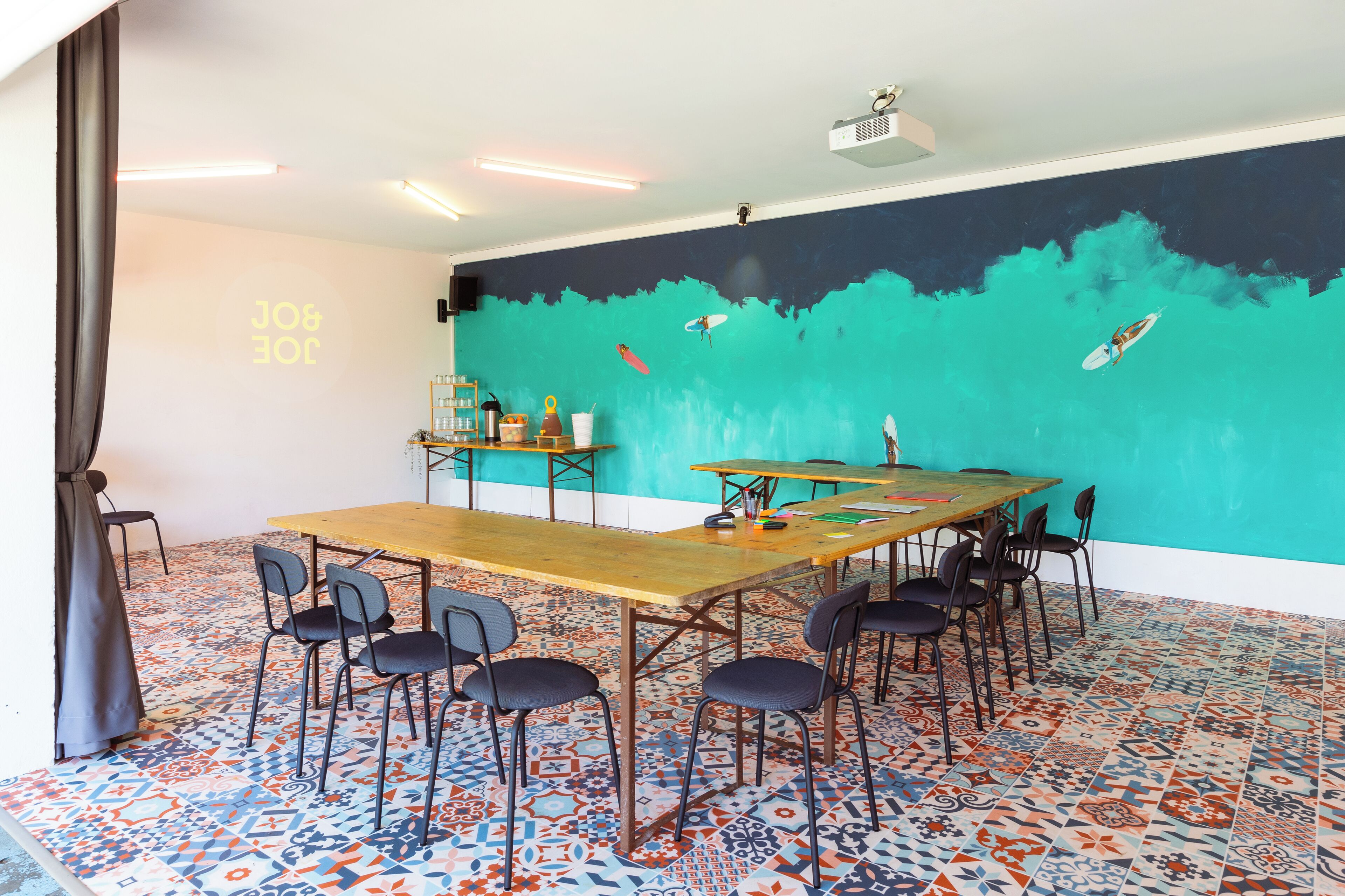 Ein Konferenzraum mit großem Tisch, Stühlen, einem Projektor und einer Wandmalerei von Surfern.