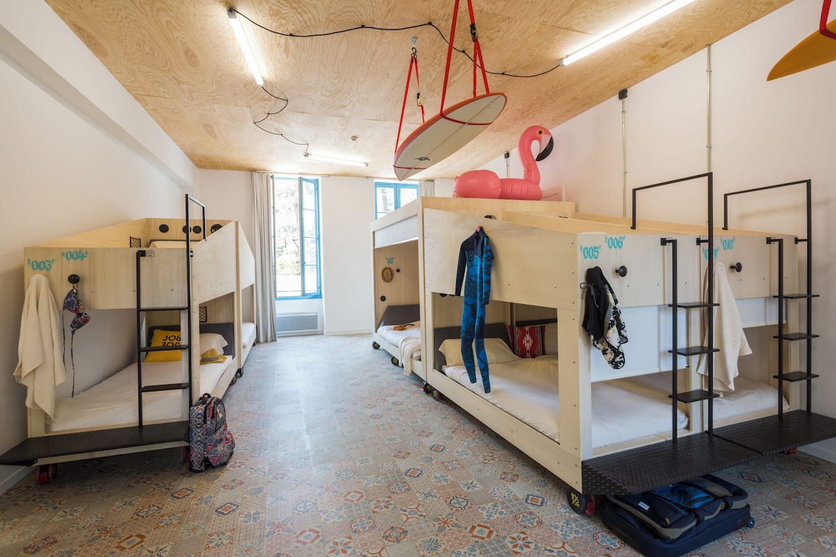 Ein Schlafsaalzimmer mit Etagenbetten, einem gemusterten Boden und einem Fenster mit Vorhängen.