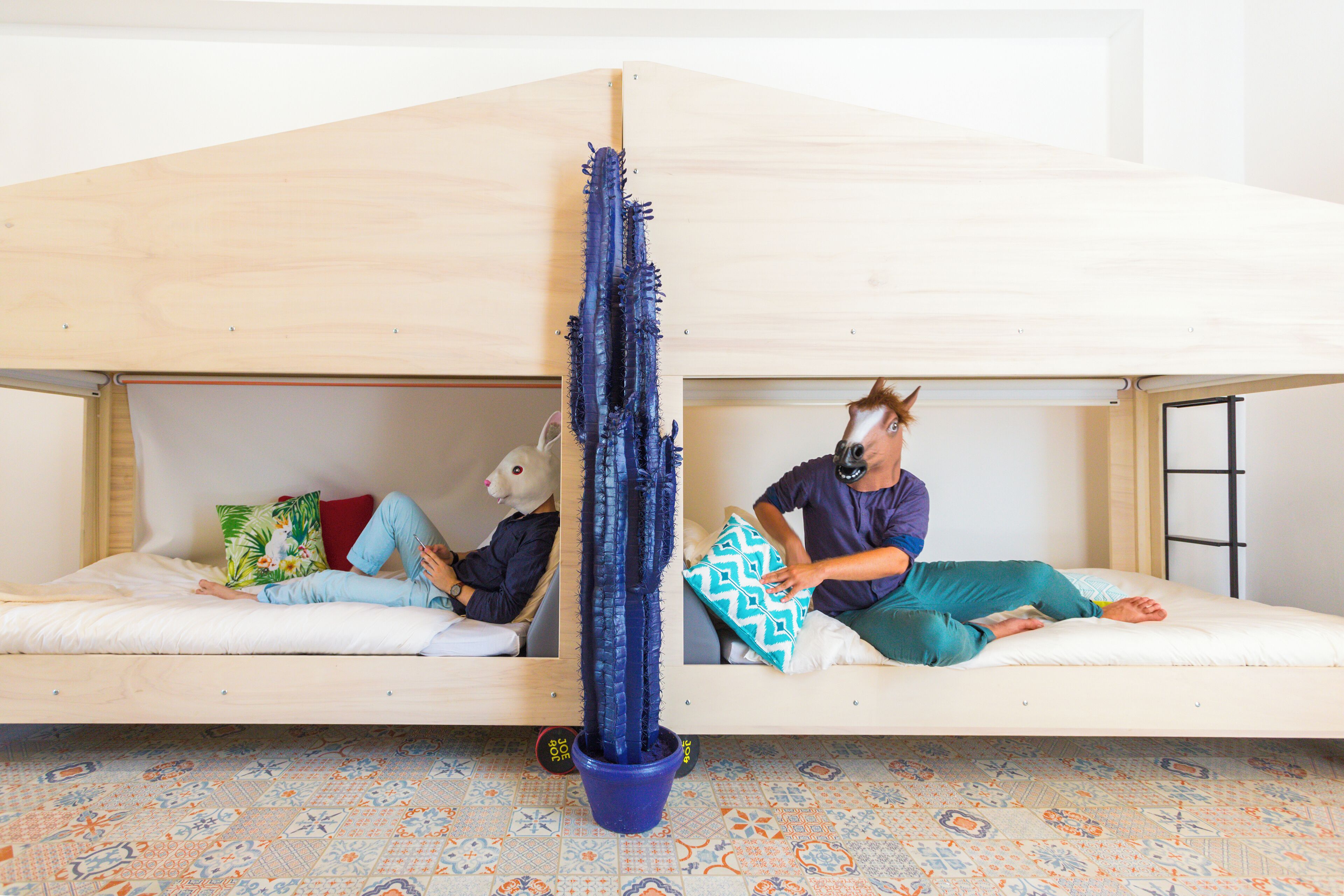 Une pièce avec deux lits superposés, un cactus bleu au centre et des carreaux de sol à motifs.