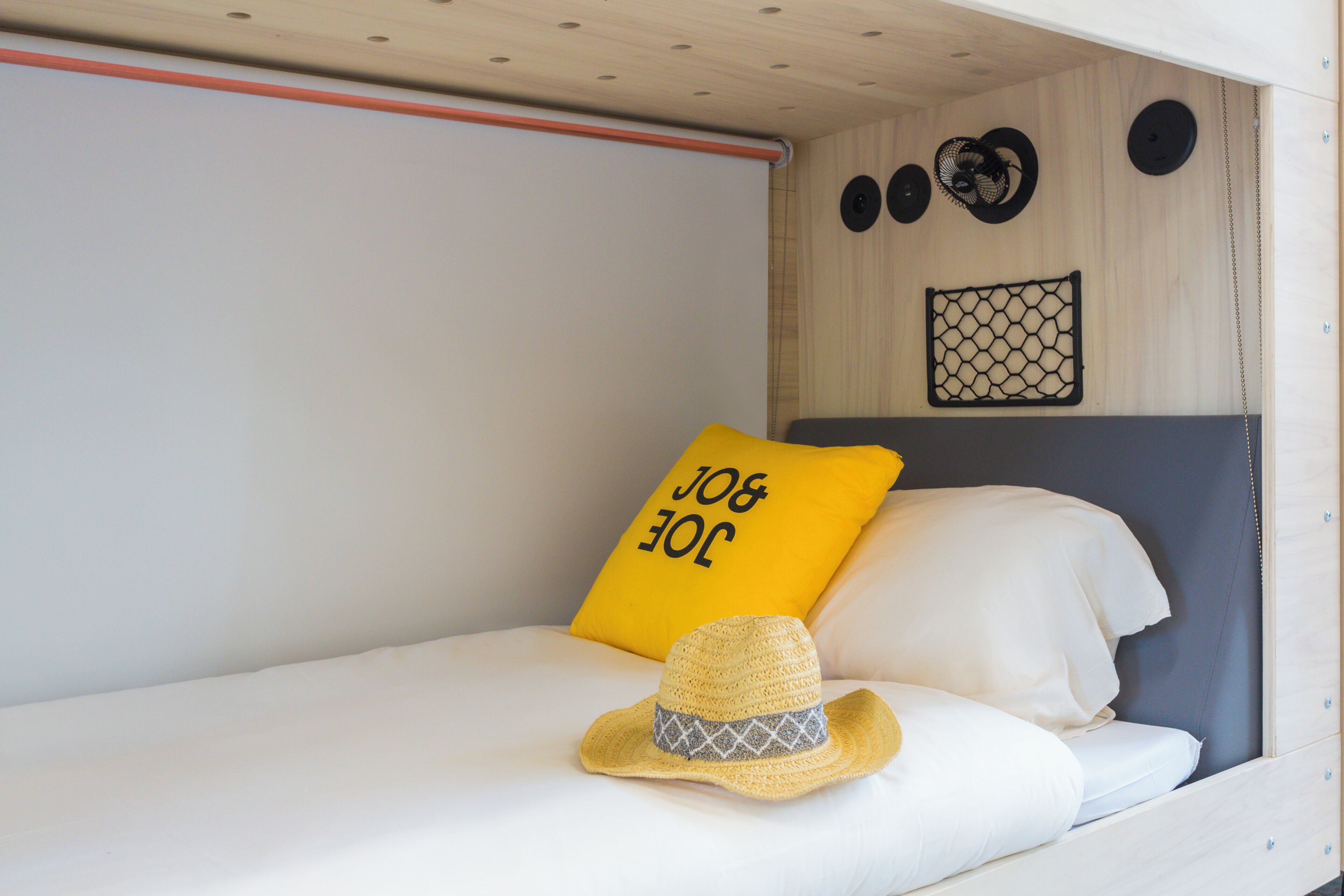 Un lit superposé avec un oreiller jaune et un chapeau de paille sur le lit du bas.