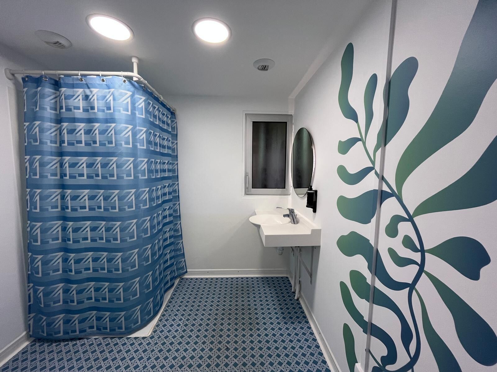 Un baño con cortina de ducha, lavamanos, espejo y piso estampado.