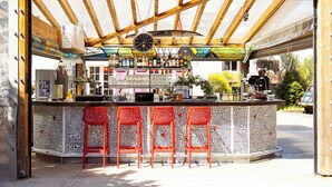 An outdoor bar with a patterned counter and red chairs.