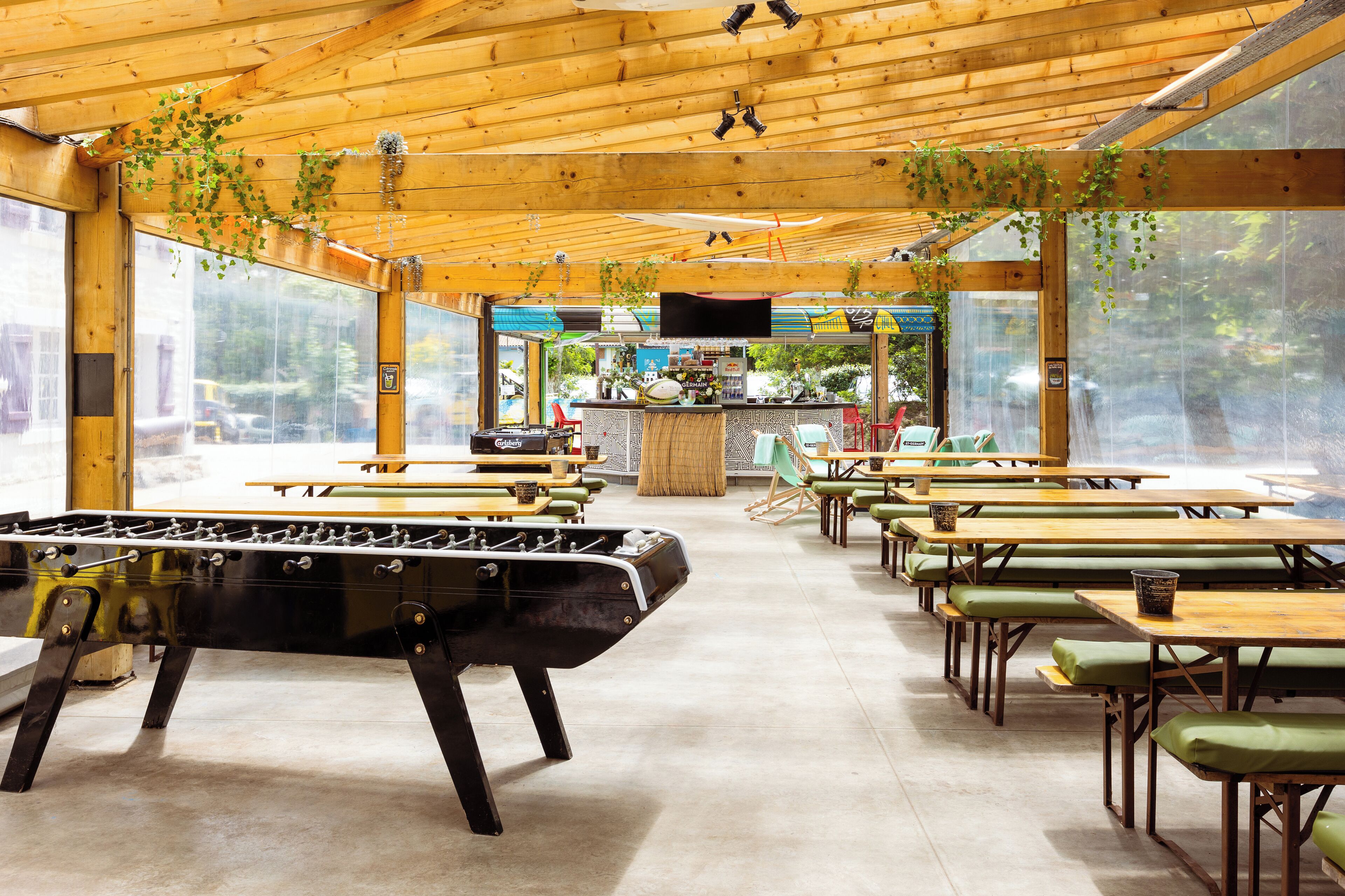 Ein geräumiger Innenbereich mit Holztischen und -stühlen, einem Tischfußballtisch und einer Bar mit Theke und Sitzgelegenheiten.