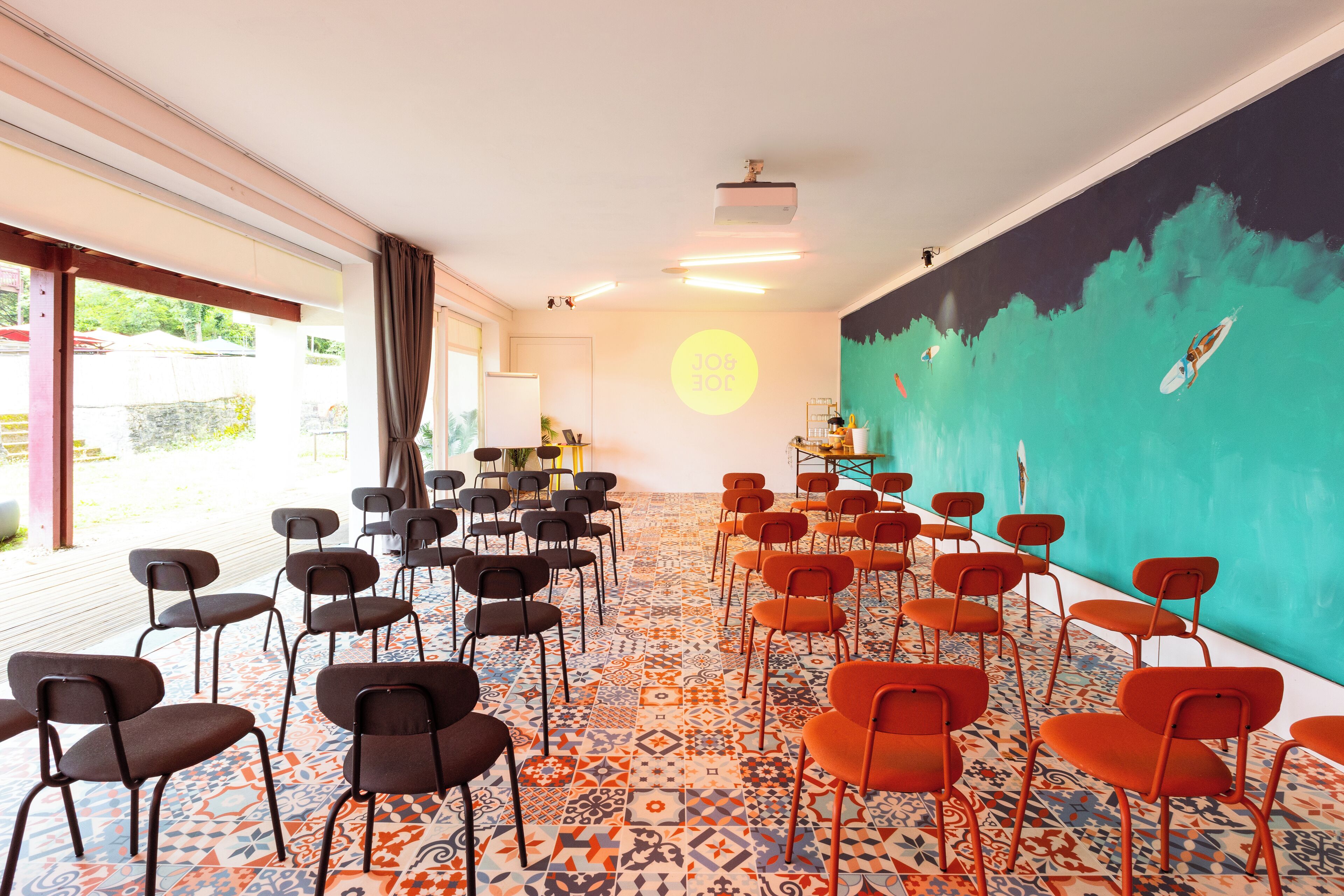 Un salón de conferencias con filas de sillas, un proyector y un mural de colores.