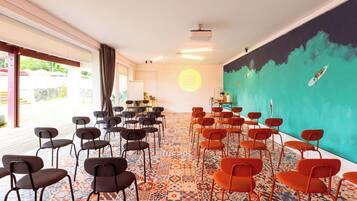 Un salón de conferencias con filas de sillas, un proyector y un mural de colores.