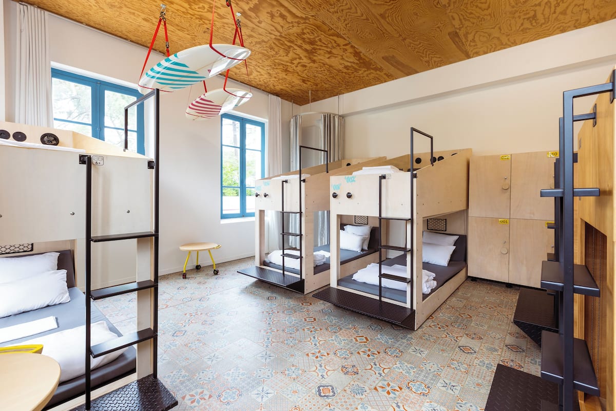 Ein Schlafsaalzimmer mit Etagenbetten, einem kleinen Hocker und einem Fenster mit Vorhängen.
