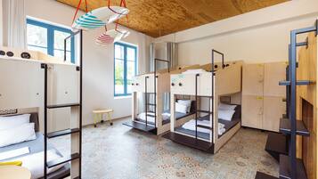A dormitory room with bunk beds, a small stool, and a window with curtains.