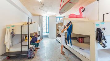 A dormitory room with bunk beds, a ceiling-mounted surfboard, and a pink flamingo decoration.