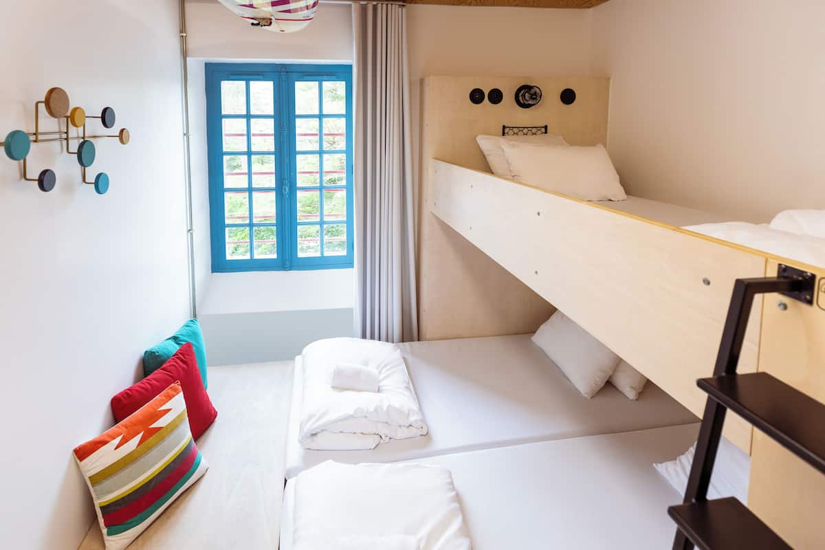 Ein Zimmer mit Etagenbett, einem Fenster mit blauen Läden und einer Wandleuchte.