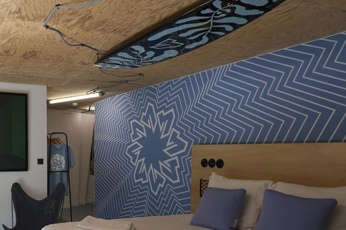 Ein Schlafzimmer mit Bett, Stuhl, Wand mit Muster und Decke mit freiliegenden Balken.